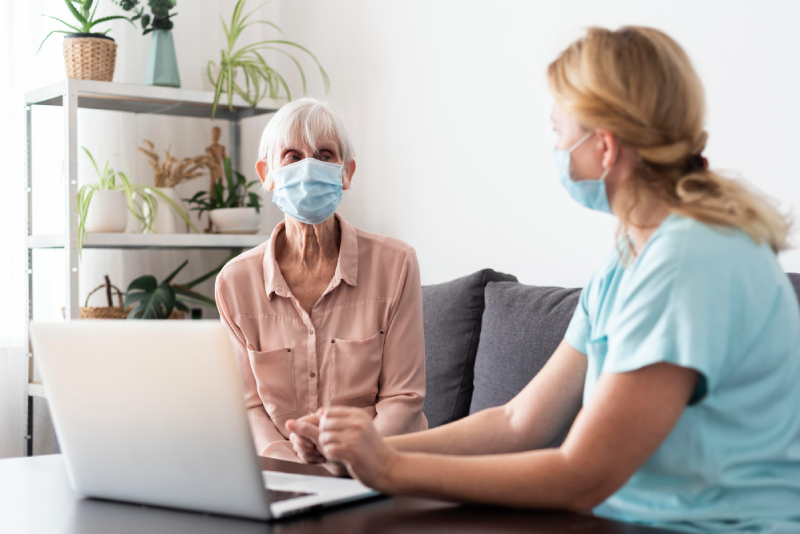 female-nurse-older-woman-conversing-laptop-nursing-home